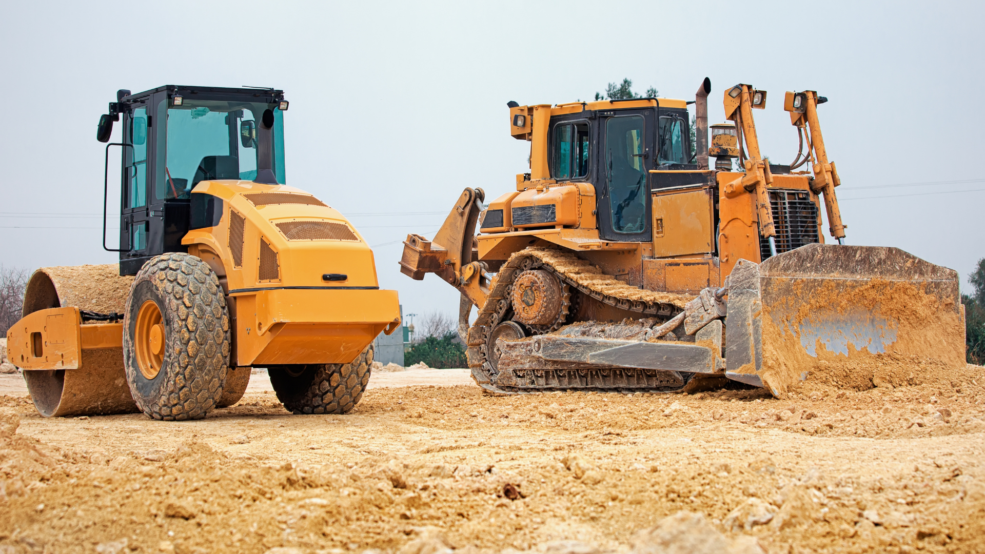 A couple of bulldozers sitting on top of a dirt field