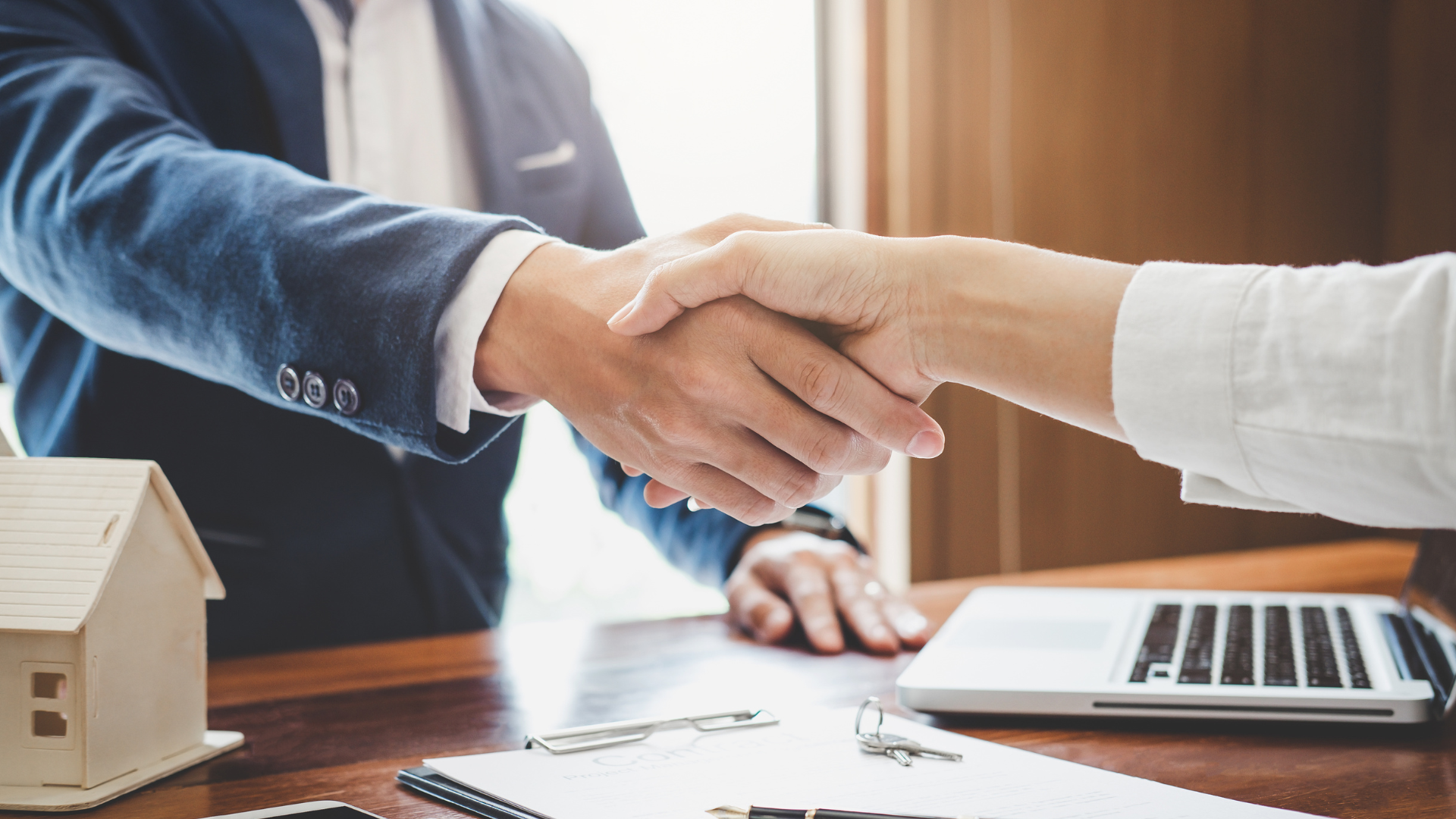 Two people shaking hands in front of a laptop